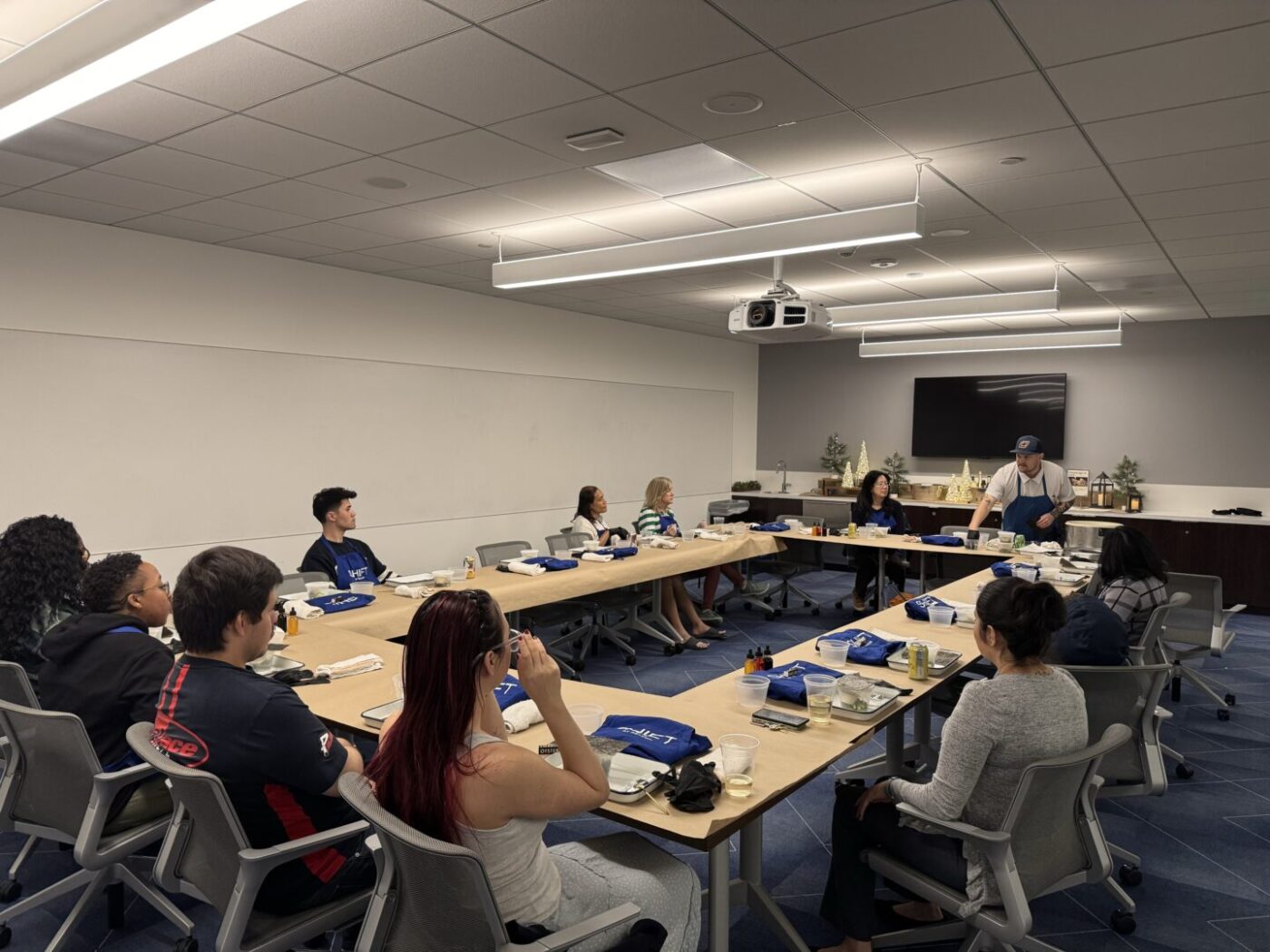 Conference tables in U-Shape with workshop materials on them. Man in apron standing behind the tables in a conference room.